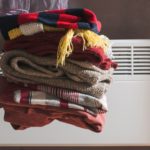 someone holding winter clothing in front of a heater