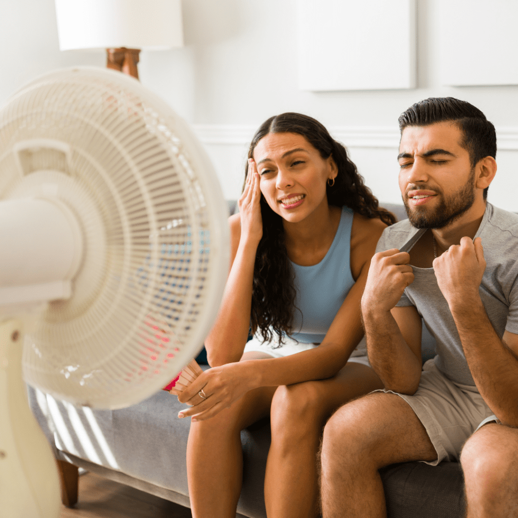 A couple sitting in front of a fan trying to cool off